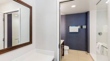 A modern bathroom with a white countertop, a glass shower enclosure, and a dark blue wall.