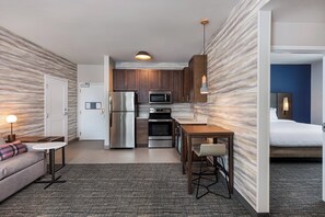 A compact hotel room with a kitchenette, a sofa, a small dining table, and a bed.