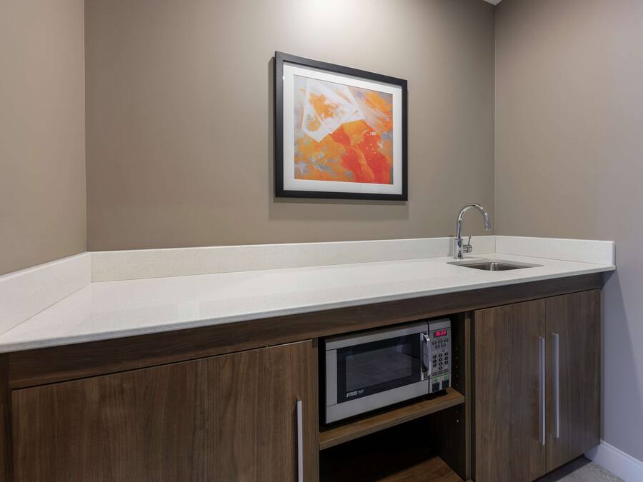 A kitchen with a white countertop, a stainless steel sink, a microwave, and wooden cabinets.