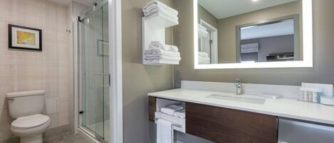 A modern bathroom with a glass shower, a toilet, a sink with a mirror, and neatly folded towels on a shelf.