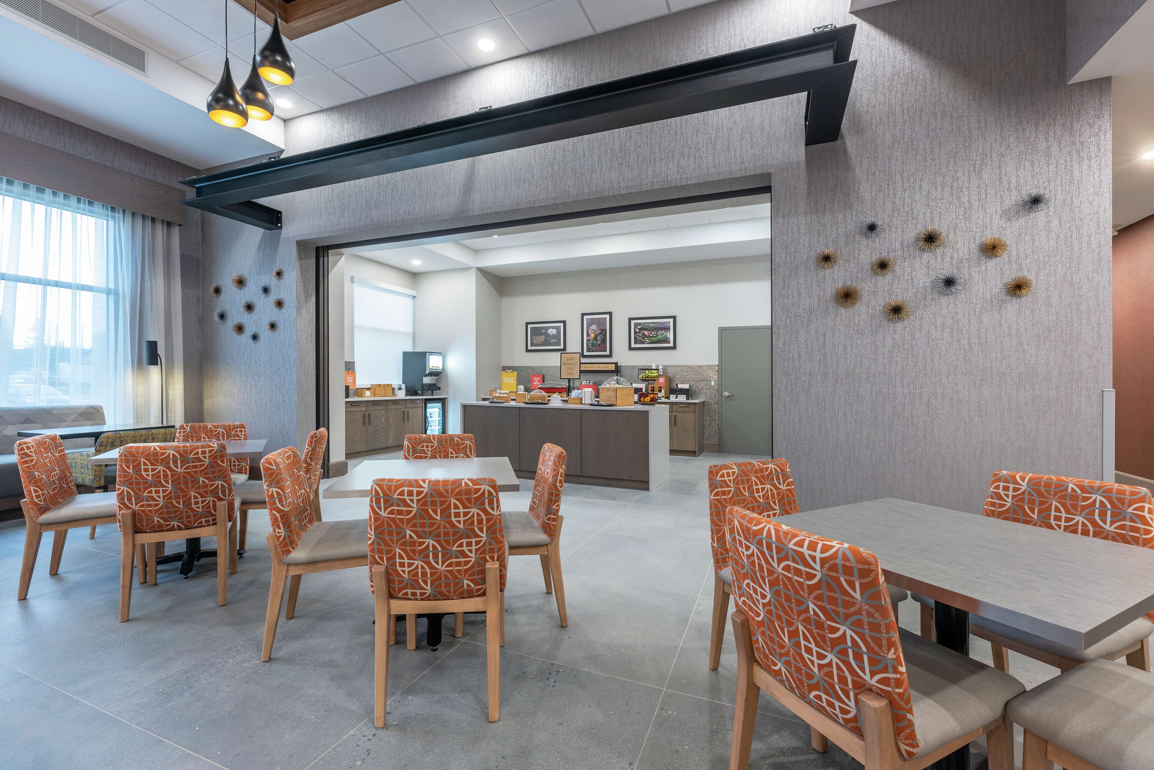 A modern dining area with a long table and chairs, a kitchen in the background, and decorative wall art.