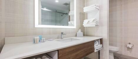 A modern bathroom with a large mirror, dual sinks, a toilet, and a shower area.