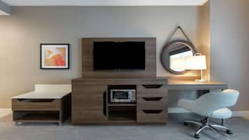 A modern hotel room with a flat-screen TV, a desk with a lamp, a microwave, and a comfortable chair.