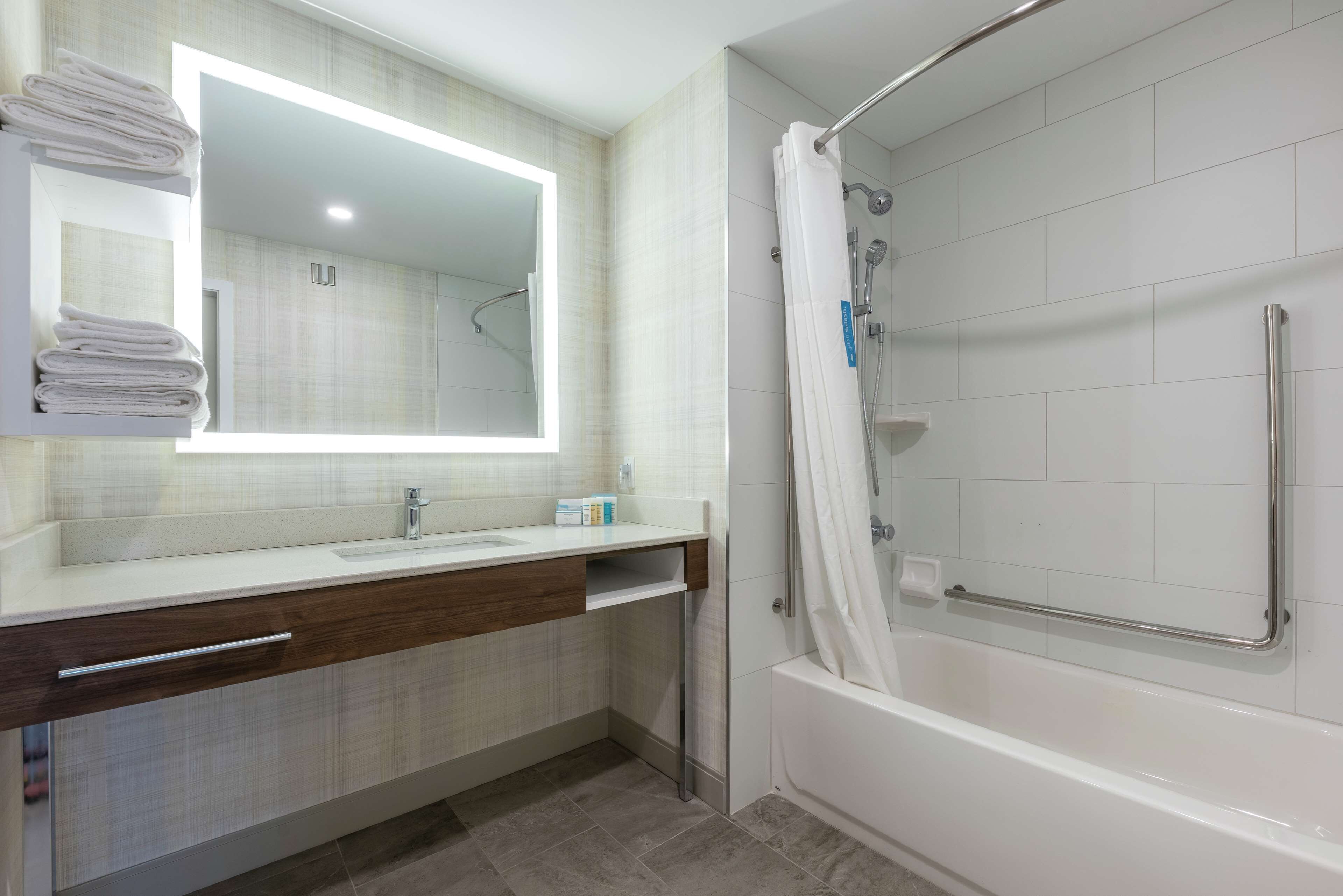Een moderne badkamer met een grote spiegel, witte tegels, een badkuip en een douchehoek.