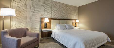 A hotel room with a bed, a chair, two bedside tables with lamps, and a patterned wall.