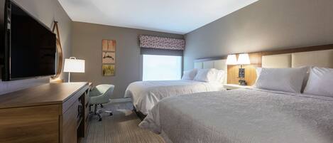 A hotel room with two beds, a desk, a chair, a TV, and a window.
