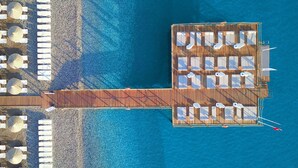 Vue aérienne d’un complexe hôtelier situé en bord de mer, avec une jetée en bois reliant les deux parties de l’établissement.