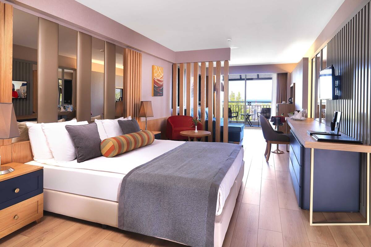A hotel room with a bed, bedside tables, a desk, and a balcony with a view.
