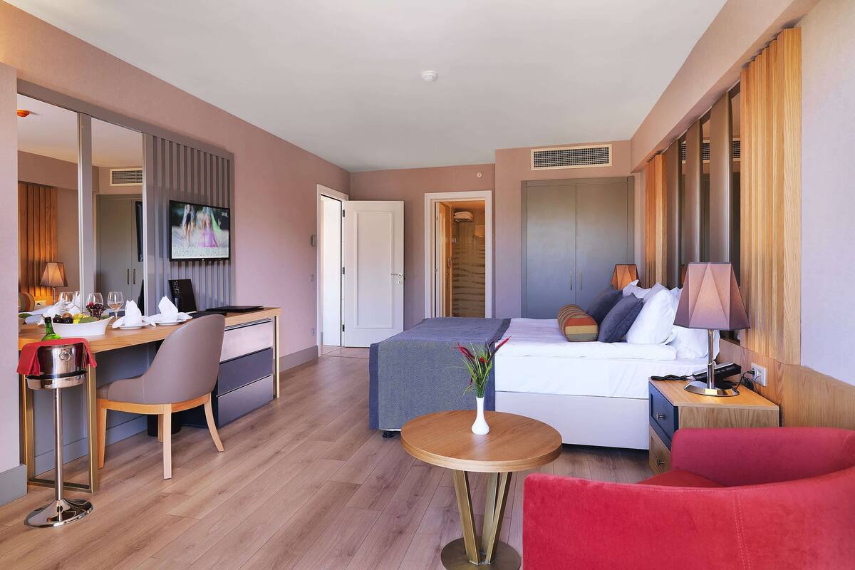 A hotel room with a bed, desk, chair, and a small table with a vase.