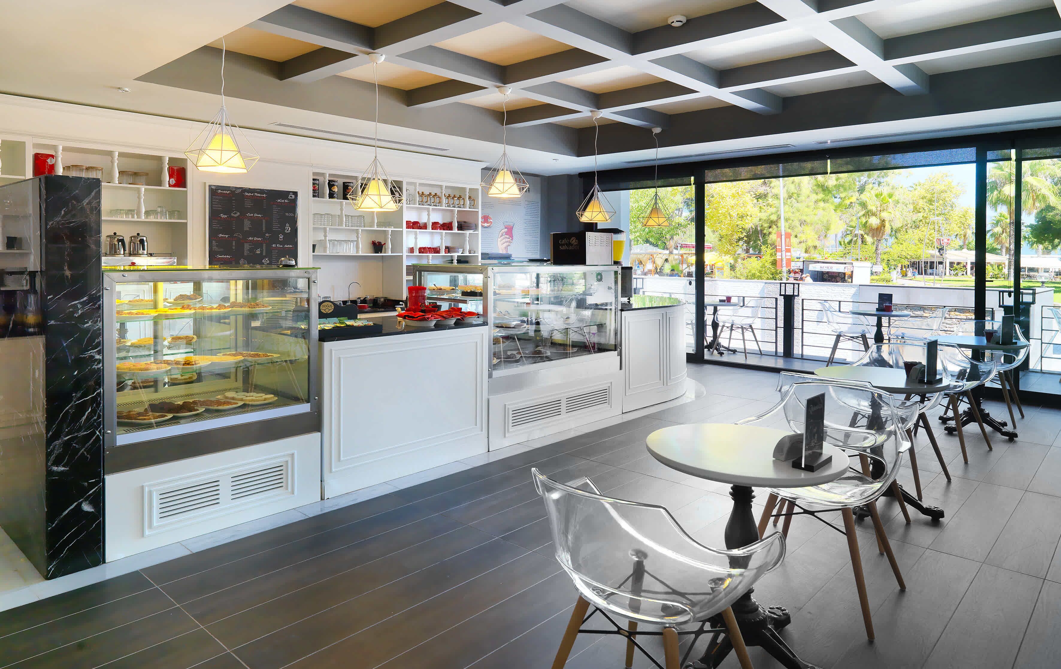 Un café moderno con un expositor de vidrio, muebles blancos y sillas traslúcidas.