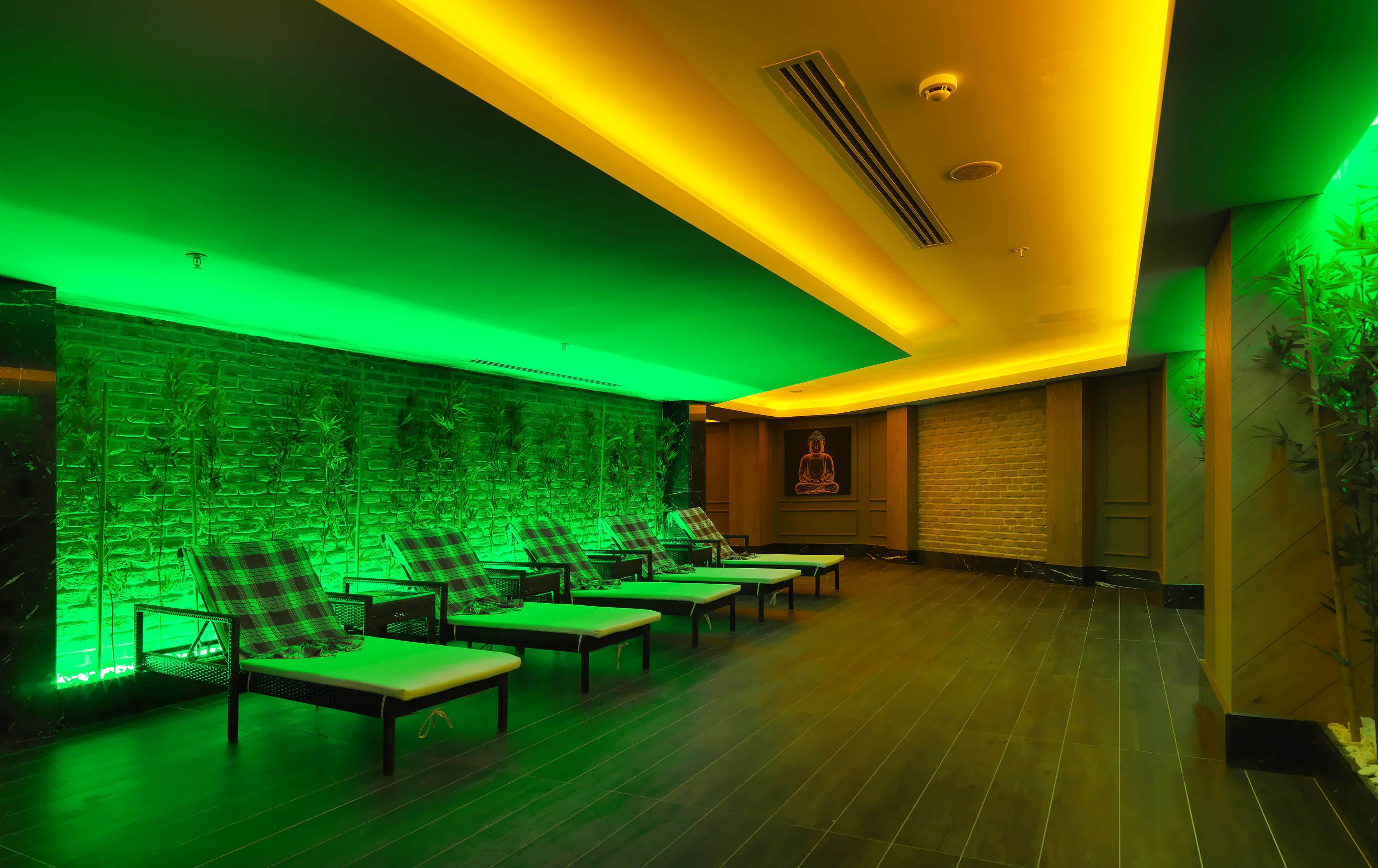 Un cuarto de spa con iluminación ambiental verde, una pared de ladrillo y varias mesas de masaje con sillas.