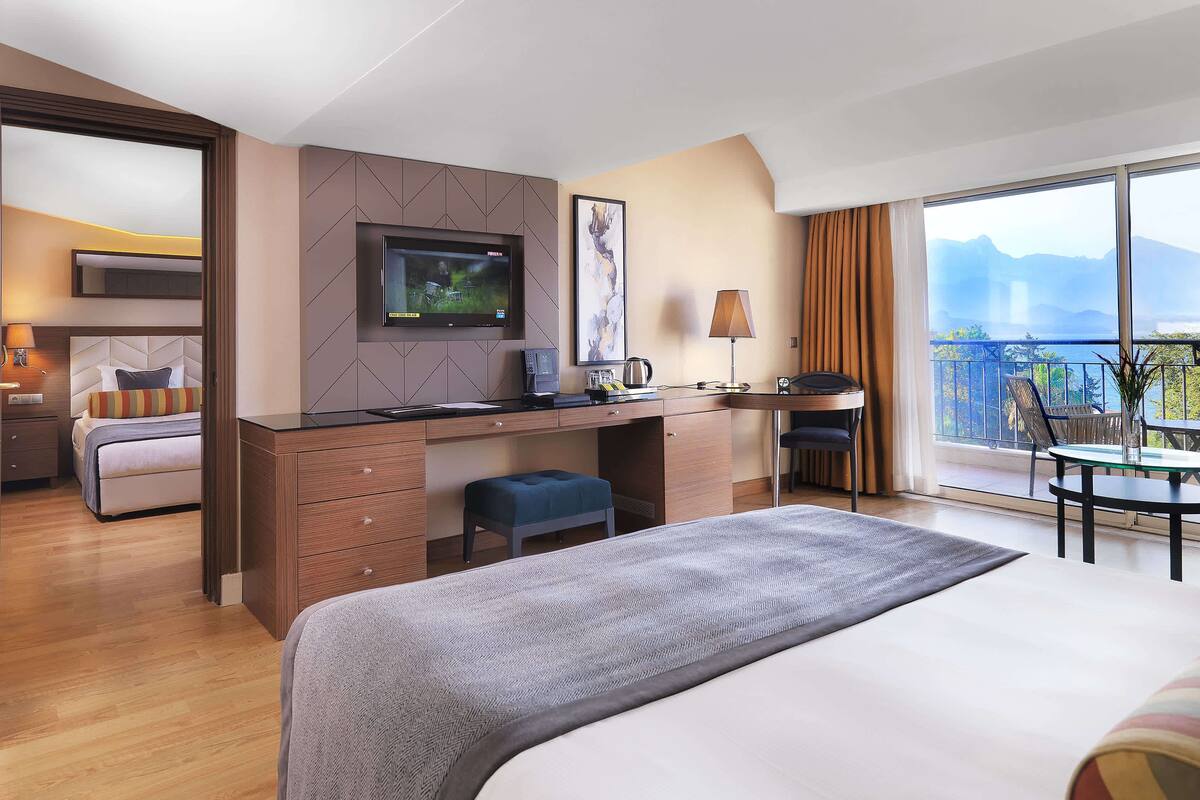 A hotel room with a bed, a desk, a chair, a TV, and a balcony with a view.