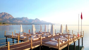 Une jetée en bois, agrémentée de chaises longues et de parasols, qui offre une vue sur un lac paisible, avec des montagnes en toile de fond.