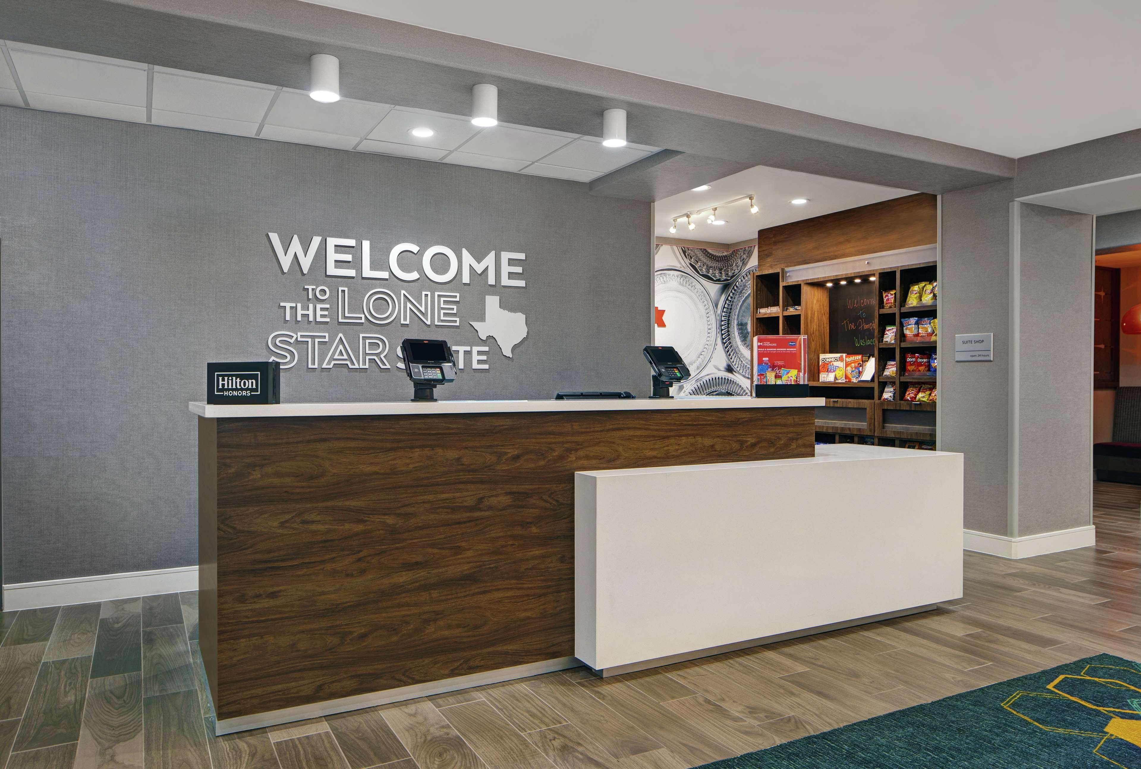 A hotel reception desk with a 'Welcome to the Lone Star' sign, a 'Hilton Honors' badge, and a 'Suite Shop' sign.