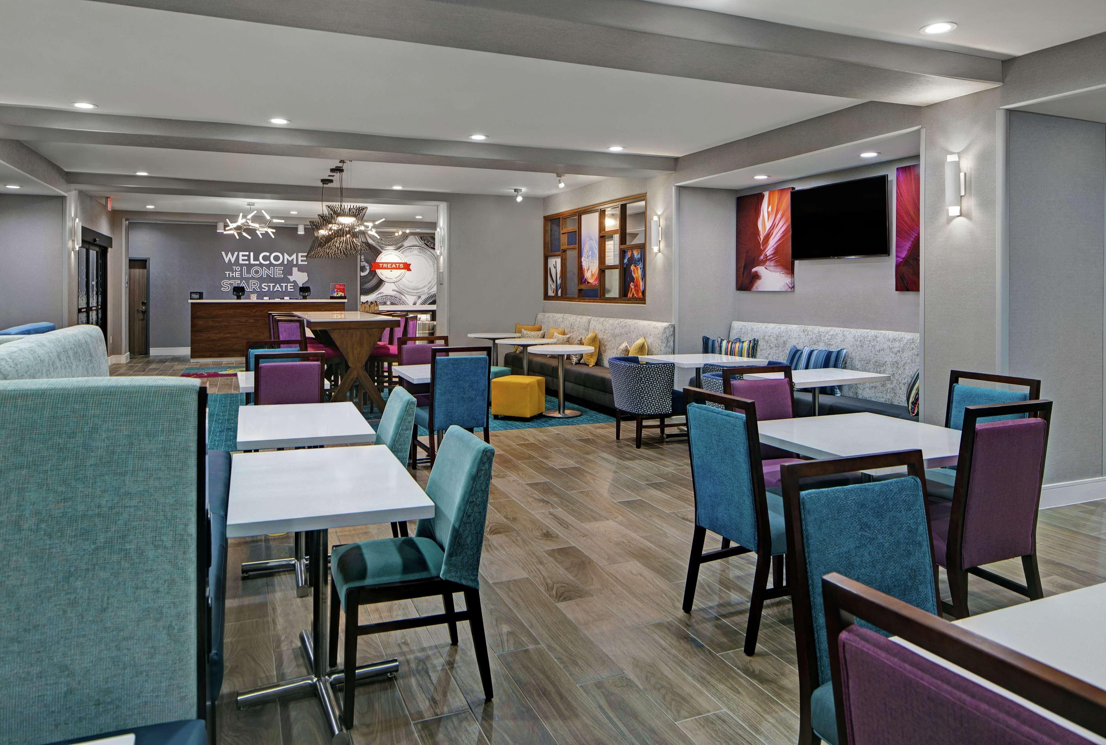 Een moderne hotel lobby met een receptiebalie, zithoeken en een aan de muur bevestigde televisie.
