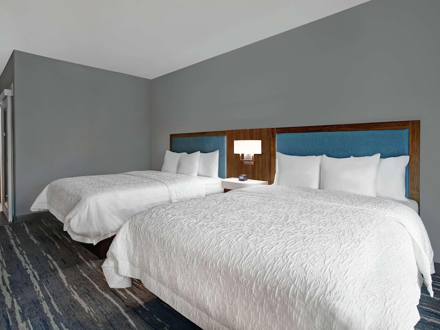Habitación de hotel con dos camas, un cabecero azul, una mesita de noche con lámpara y una alfombra a rayas.