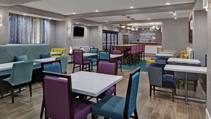 A modern restaurant with a mix of booths and tables, a bar area, and a welcoming sign. - Hampton Inn Weslaco (Weslaco)