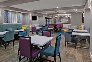 A modern restaurant with a mix of booths and tables, a bar area, and a welcoming sign. - Hampton Inn Weslaco (Weslaco)