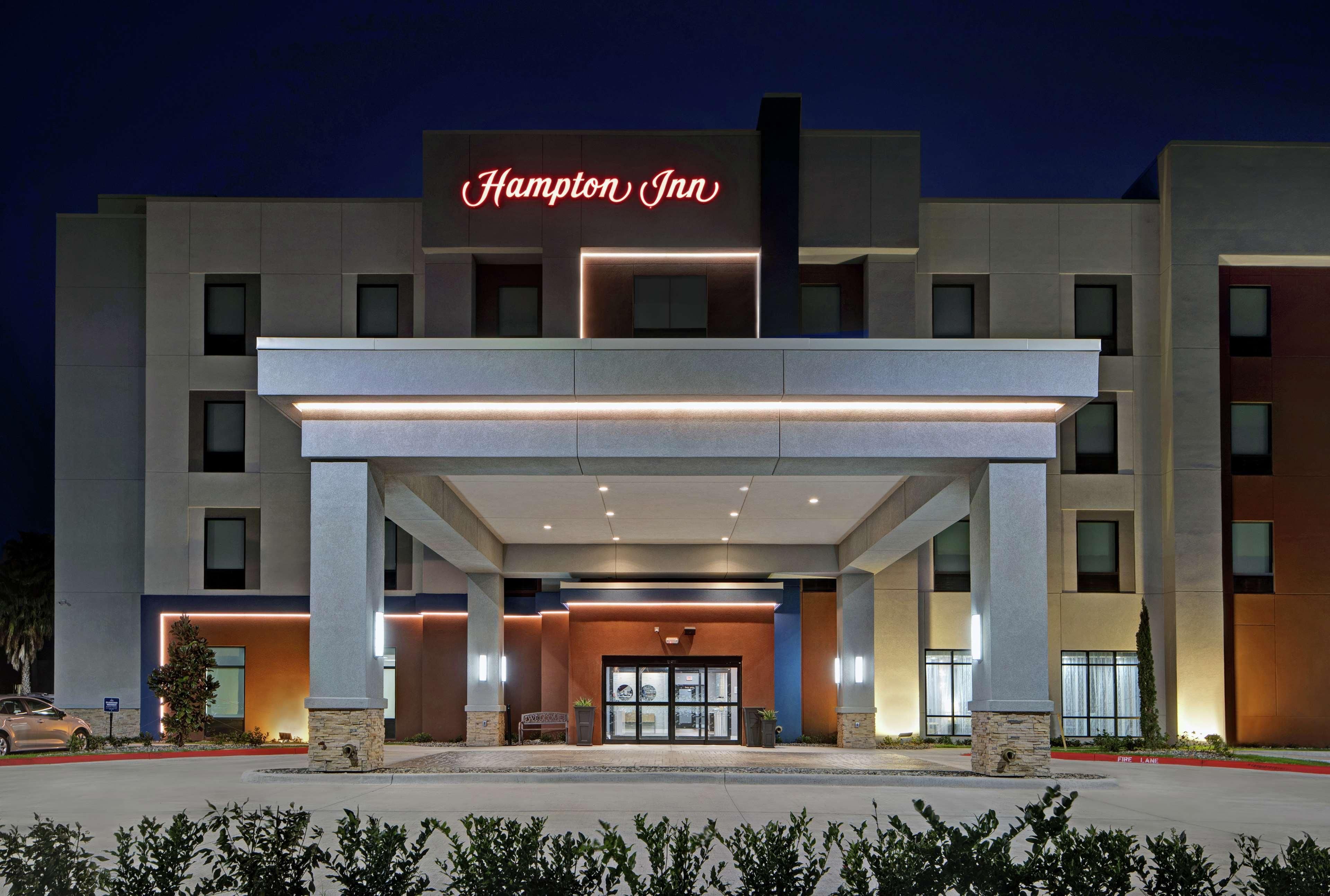 Um hotel Hampton Inn com fachada moderna, grande entrada e sinalização iluminada.