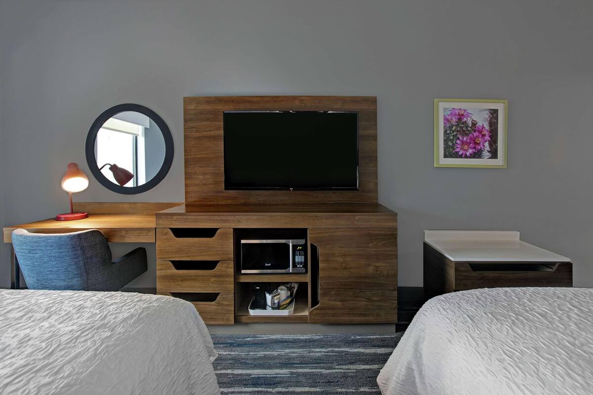 Une chambre d’hôtel équipée d’un meuble en bois pour la télévision, d’un téléviseur à écran plat, d’un bureau avec une lampe, d’un four à micro-ondes et d’une petite table de chevet.