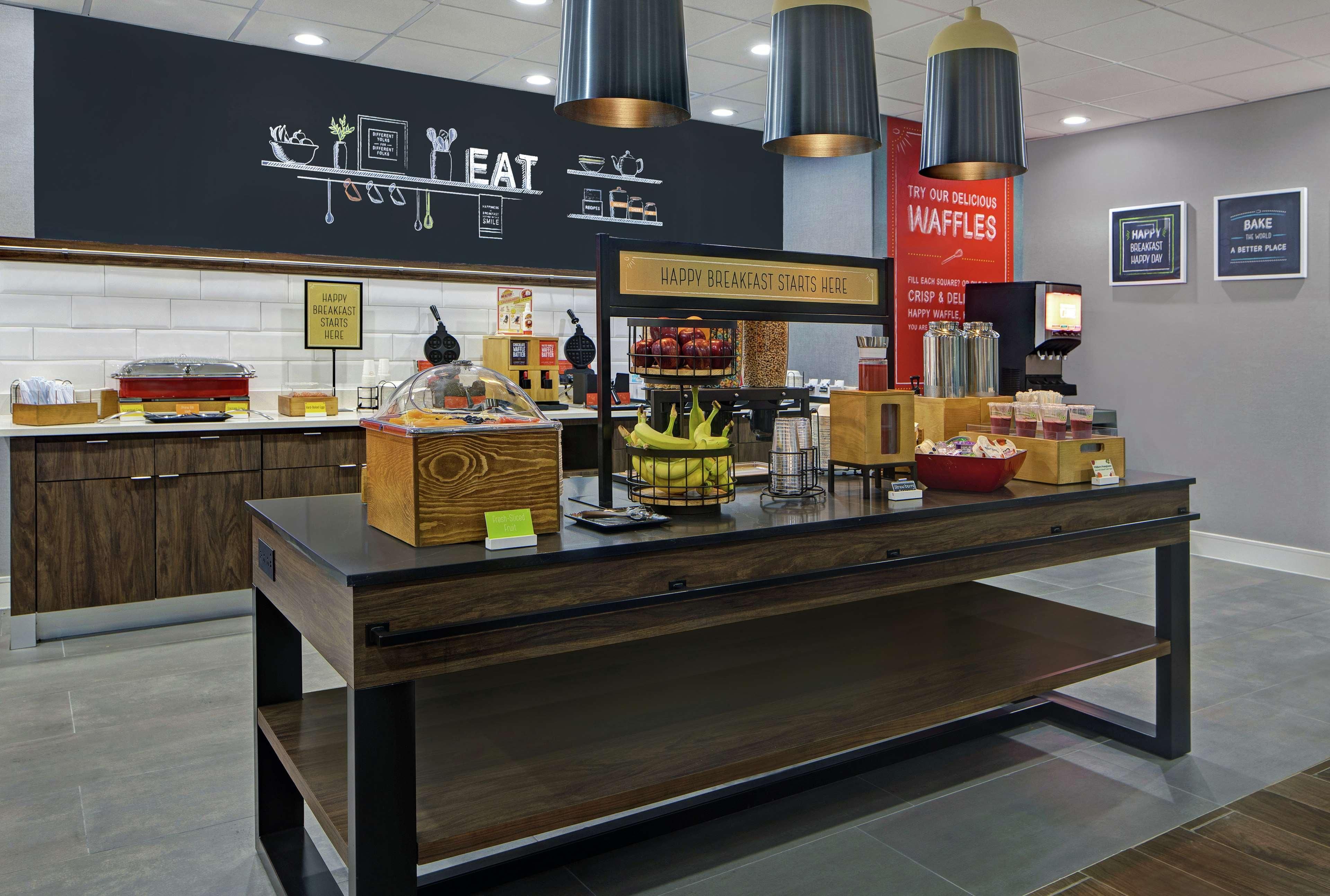 A breakfast buffet area with a sign that reads "HAPPY BREAKFAST STARTS HERE" and another sign advertising waffles.