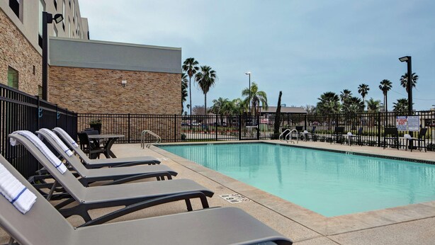 A pool area with lounge chairs, a table, and a stone building in the background. - Hampton Inn Weslaco (Weslaco)