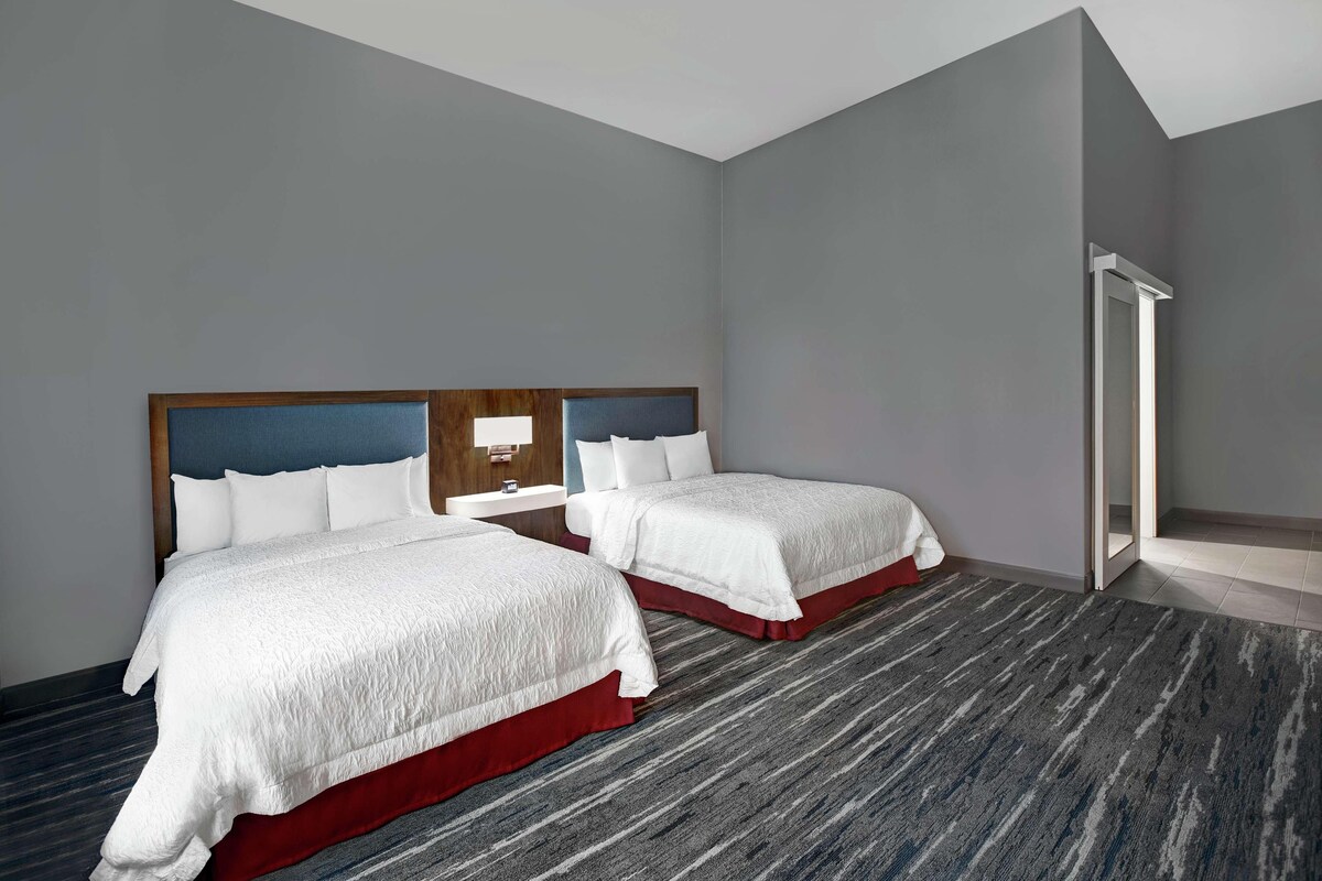Une chambre d’hôtel avec deux lits, une table de chevet, un miroir et un espace douche.