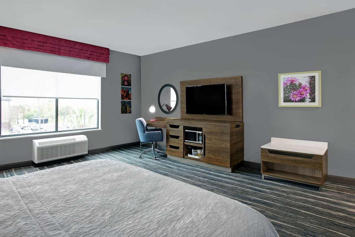 Une chambre moderne avec un grand lit, un bureau, une télévision et une fenêtre donnant sur l’extérieur.