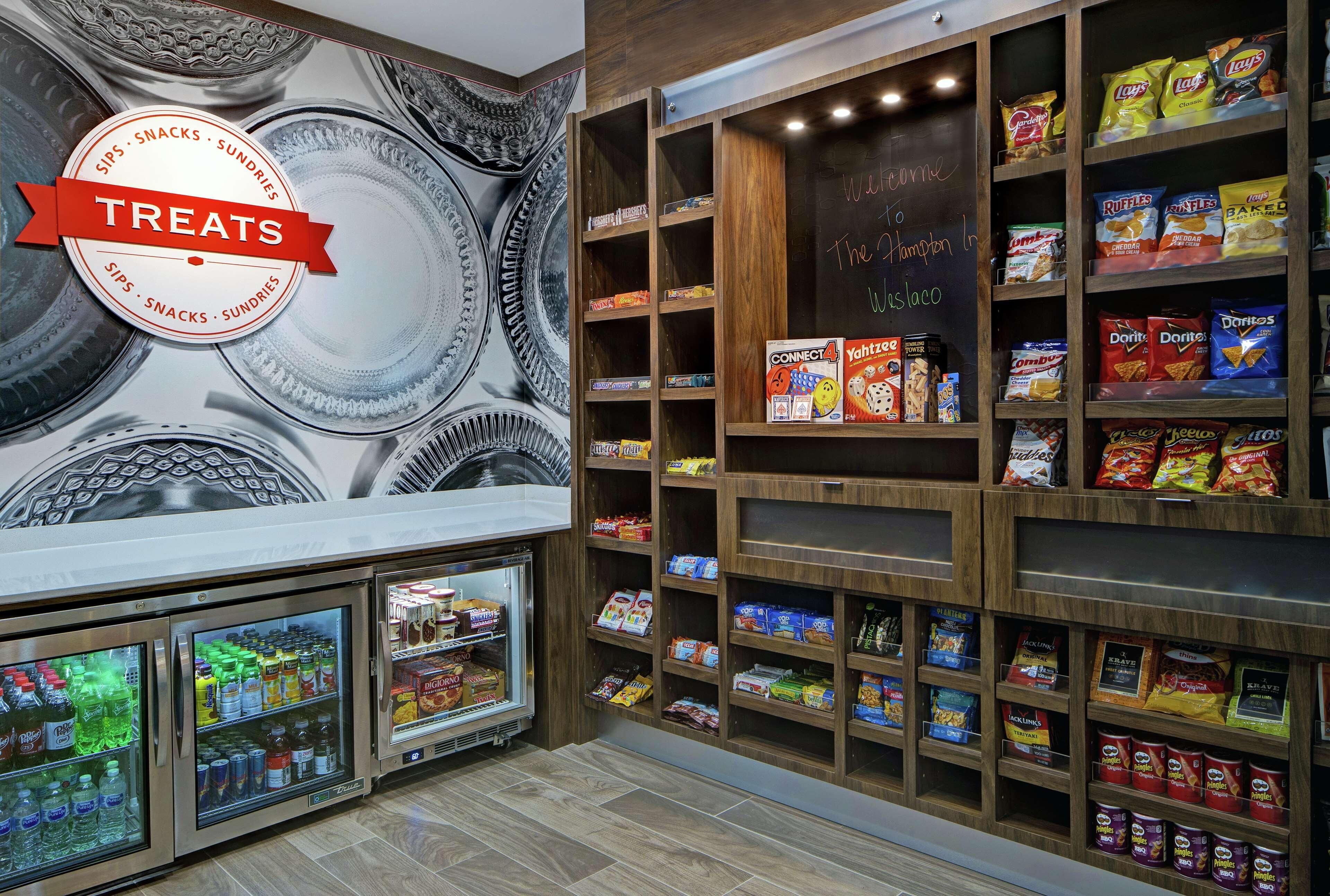 A snack display area with various chips and snacks, a refrigerated section with beverages, and a chalkboard with a welcome message.