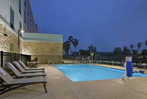 A pool area with lounge chairs, a stone wall, and palm trees in the background. - Hampton Inn Weslaco (Weslaco)