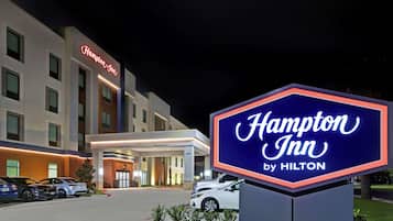 A Hampton Inn by Hilton hotel with a clear entrance, a parking lot with several cars, and a well-lit signboard.