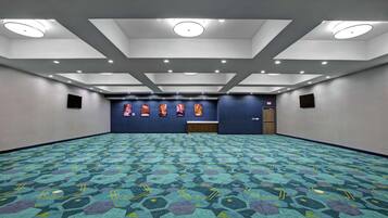 A conference room with a patterned carpet, recessed ceiling lights, and a row of framed pictures on the back wall.
