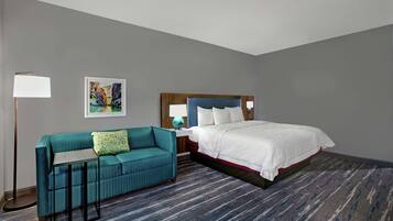 A hotel room with a bed, a sofa, a lamp, and a picture on the wall.