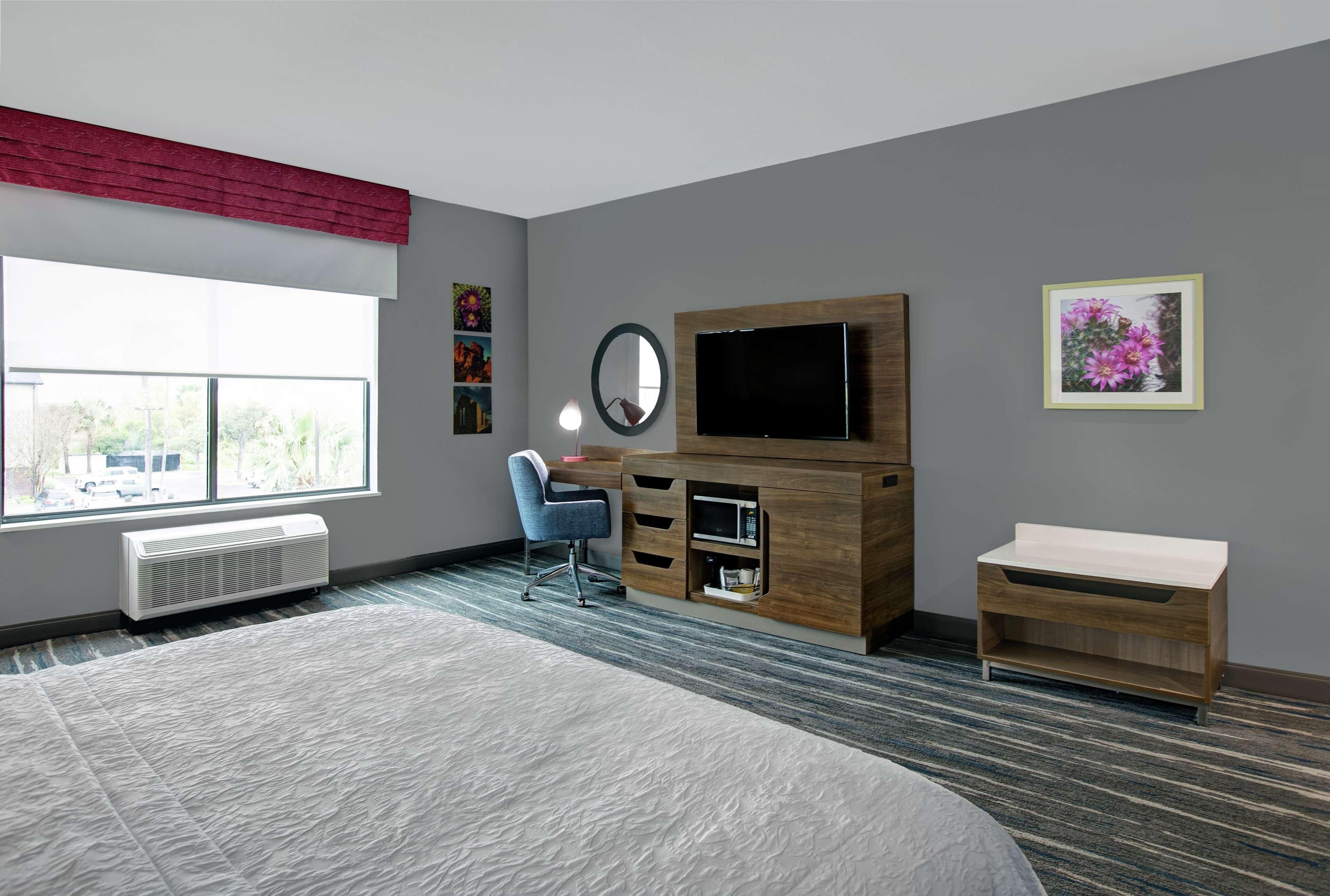 A modern bedroom with a large bed, a desk, a TV, and a window with a view of trees.