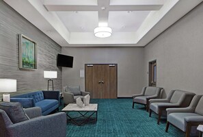A hotel room with a blue sofa, grey armchairs, a coffee table, a flat-screen TV, and a wooden door. - Hampton Inn Weslaco (Weslaco)