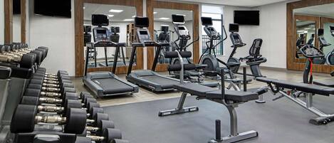 Een fitnessruimte met loopbanden, elliptische trainers en gewichten.