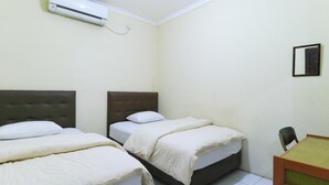 A small, clean room with two beds, a desk, and an air conditioning unit on the wall. - Guest House Samarinda (Samarinda)