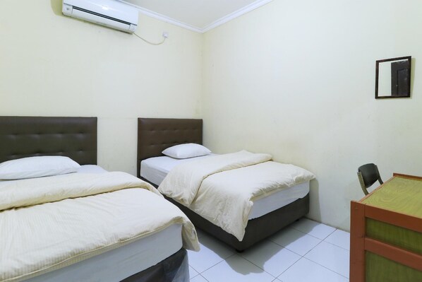 A small, clean room with two beds, a desk, and an air conditioning unit on the wall. - Guest House Samarinda (Samarinda)