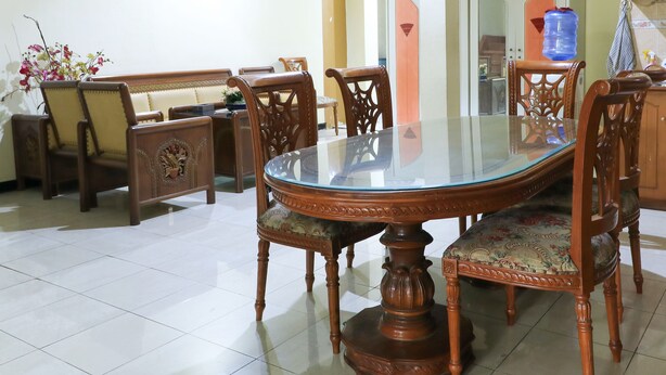 A dining area with a glass-top table surrounded by wooden chairs with intricate carvings. - Guest House Samarinda (Samarinda)