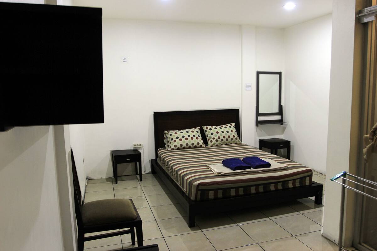 A bedroom with a bed, a chair, a TV mounted on the wall, and a small table.