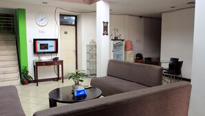 A hotel lobby with a sofa, a coffee table, a television, a refrigerator, and a staircase. - Saidah Guest House (Bandung)
