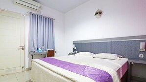 Une chambre d’hôtel équipée d’un lit, d’un bureau, d’une chaise, d’une table de chevet et d’un climatiseur fixé au mur.