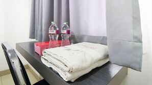 Un lit bien fait, avec une serviette blanche pliée et deux bouteilles d’eau posées sur une table de chevet.