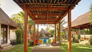 A covered outdoor seating area with a pool in the background. - Kandahill Bali (Pecatu)