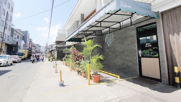 A hotel named 'Palem' with a covered entrance, potted plants along the sidewalk, and parked cars on the street. - Hotel Palem (Bandung)