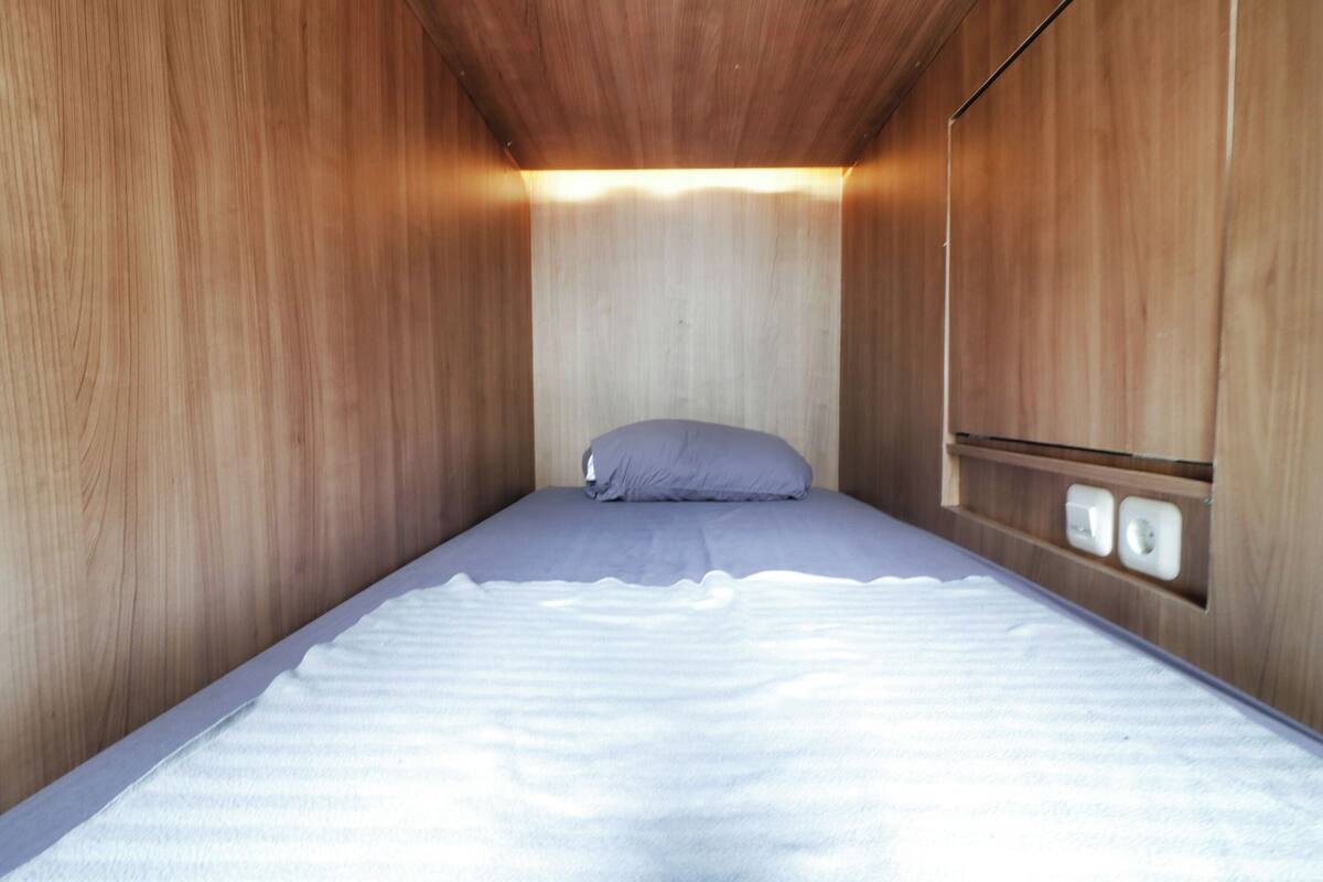 A small, single-bed room with wooden walls and a simple bed.