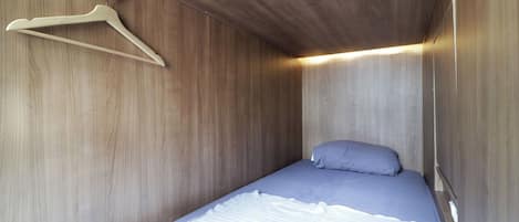 Una habitación pequeña con cama individual, paredes de madera y un perchero de madera en la pared.