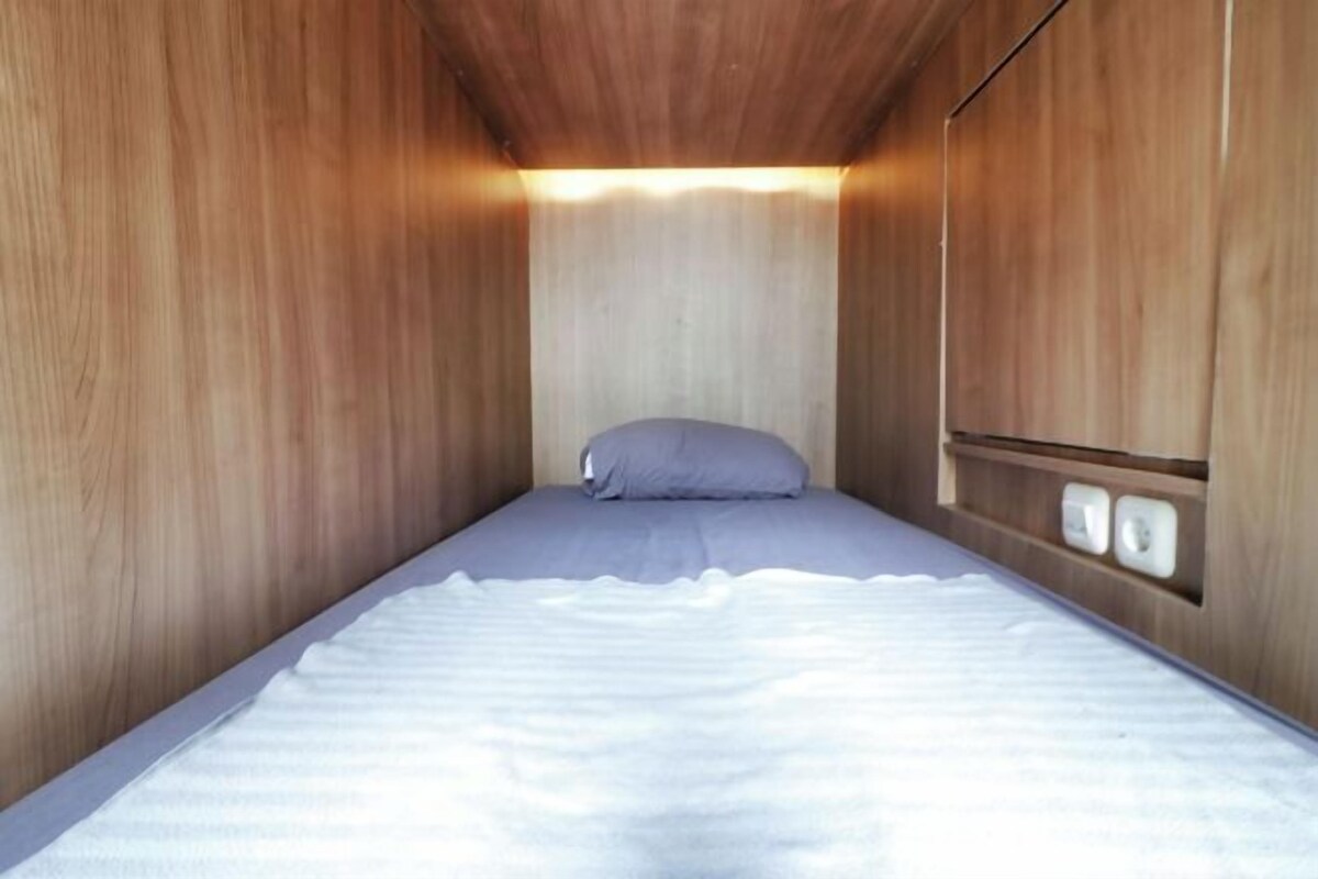 Habitació petita amb un llit individual, parets de fusta i un disseny senzill i net.
