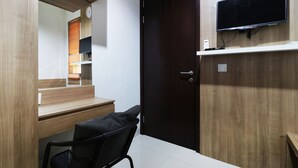 A modern office space with a wooden desk, a black office chair, a closed dark wooden door, and a mounted flat-screen TV. - Oliver's Guest House (Pagedangan)