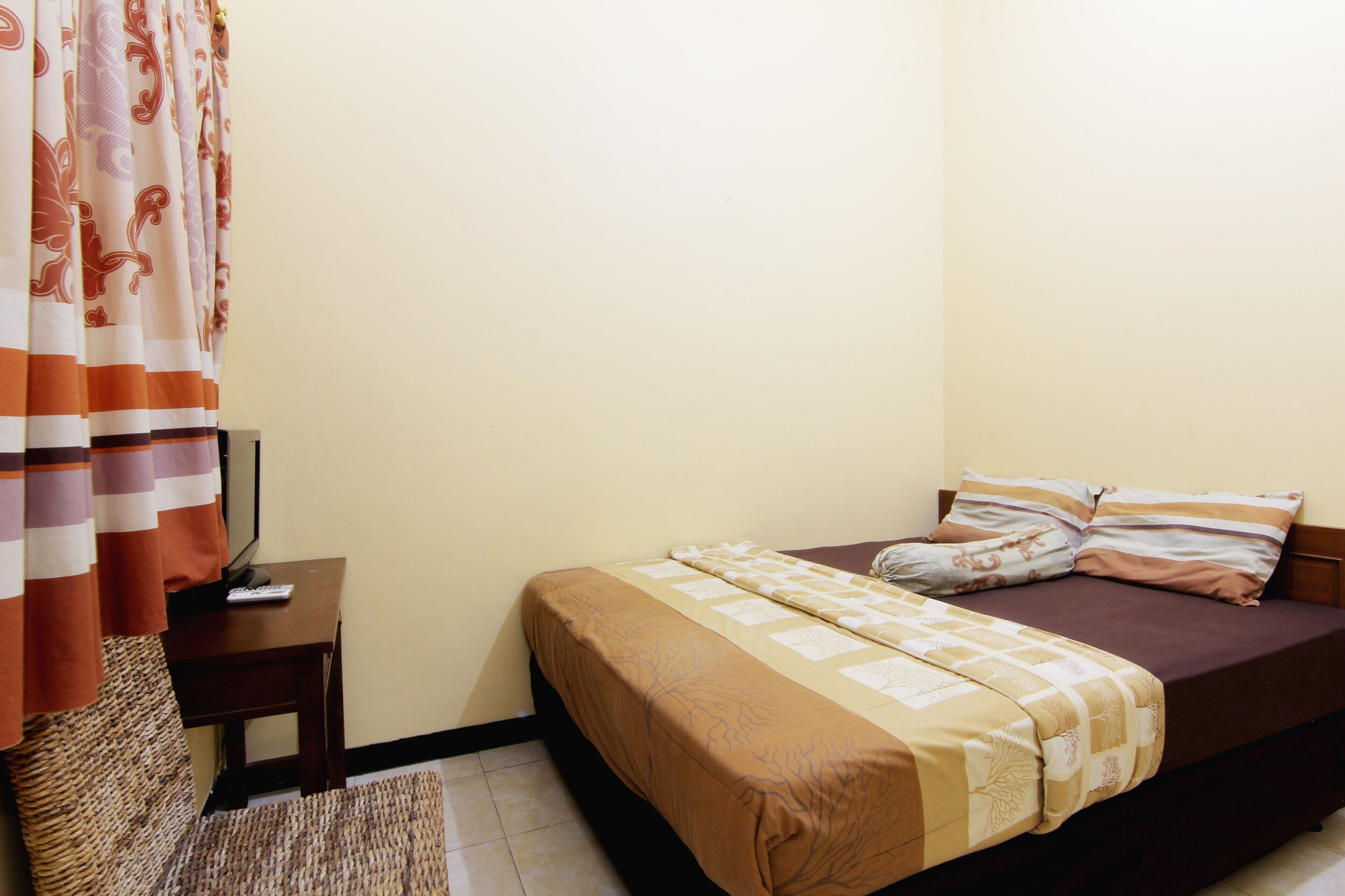 A bedroom with a bed, a bedside table, a lamp, a chair, and a patterned curtain.